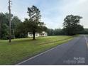 A long, green lawn surrounds a cozy, single-story home, with a road in the foreground and forest in the background at 40287 Palmerville Rd, New London, NC 28127