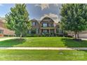 Brick two-story home with manicured lawn, lush trees and shrubbery under a blue sky with puffy white clouds at 3913 Widgeon Way, Waxhaw, NC 28173