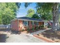 An exterior view of a one-story brick home showcasing the driveway, landscaping, and surrounding trees at 4526 Longwood Dr, Charlotte, NC 28209