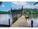 Wooden dock leading to calm lake waters, surrounded by lush greenery and a picturesque horizon at 9763 Pine Tree Ln, Norwood, NC 28128