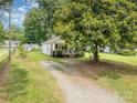 A cozy, light-colored house nestled among lush trees with a gravel driveway at 201 Oakland Dr, Lowell, NC 28098