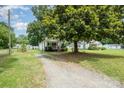 A cozy, light-colored house nestled among lush trees with a gravel driveway at 201 Oakland Dr, Lowell, NC 28098