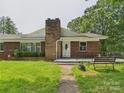 Inviting front entrance to brick ranch with stone chimney, tidy landscaping, and bench at 61 23Rd Nw St, Hickory, NC 28601