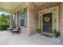 Inviting front porch with black door, colorful floral wreath, and seating for guests and enjoying the outdoors at 9801 Blackbird Hill Ln, Mint Hill, NC 28227