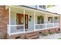 Inviting front porch with a stained wood front door with sidelights and hanging floral arrangements and painted wood railing at 110 Club Dr, Mooresville, NC 28115