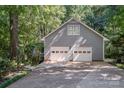 Gray home featuring an attached two-car garage with white doors surrounded by lush trees and foliage at 140 Rustic Way Ln, Mooresville, NC 28117