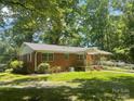 Rear exterior view of a brick home featuring a ramp and access to a well-shaded yard surrounded by trees at 2120 Marwood Ln, Albemarle, NC 28001