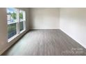 Bright, unfurnished living room featuring wood-look flooring, neutral paint, and large window with backyard view at 2382 Drake Mill Sw Ln, Concord, NC 28025