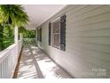 Inviting front porch with white railings, dark shutters, and a serene setting amongst trees and foliage at 1118 Brookwood Dr, Stanley, NC 28164