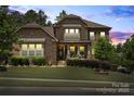 Elegant two-story home with a stone facade, manicured lawn, landscape lighting, and covered front porch at 16402 Doves Canyon Ln, Charlotte, NC 28278