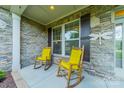 Cozy front porch with stone accents and two rocking chairs with bright yellow cushions at 6417 Loyola Ct, Mint Hill, NC 28227