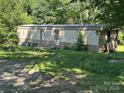 Exterior view of a mobile home, featuring a weathered facade, surrounded by tall, verdant foliage at 208/210 Damascus Rd, Gastonia, NC 28056