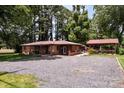 Brick home featuring a gravel driveway and outdoor covered patio, surrounded by mature trees at 835 Holshouser Rd, Rockwell, NC 28138