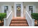 Close-up of the front door with brick steps, trimmed in white rails, a decorative wreath, and sidelight windows at 2410 Monticello Dr, Gastonia, NC 28056