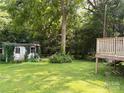 Green backyard showcasing a wooden deck and outbuilding amidst lush greenery and mature trees at 438 Faith Sw Dr, Concord, NC 28027