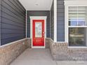 Inviting covered porch with a vibrant red front door, brick accents, and ample natural light at 1516 Respect Nw St, Concord, NC 28027