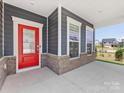 Inviting covered porch with a vibrant red front door, brick accents, and ample natural light at 1516 Respect Nw St, Concord, NC 28027