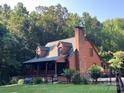 Charming log cabin with a brick chimney, dormer windows, and a covered porch nestled amongst mature trees at 485 Johnson St, China Grove, NC 28023