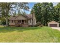 Inviting single-Gathering home with a stone chimney, front porch, mature trees, detached garage, and spacious green lawn at 544 Hicks Creek Rd, Troutman, NC 28166