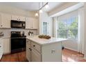 Bright kitchen showcasing a center island, black appliances, white cabinets, and a window view at 10094 Treeside Ln, Matthews, NC 28105