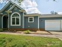 Exterior of blue home with an arched window, brick foundation, attached garage, and manicured lawn at 8323 Bedford Green Ln, Charlotte, NC 28215