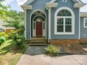Home exterior featuring a red front door with an arched window, brick foundation, and lovely landscaping at 8323 Bedford Green Ln, Charlotte, NC 28215