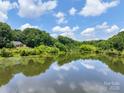 Scenic view of a tranquil pond reflecting a blue sky with puffy clouds, surrounded by lush greenery and trees at 132 General Pemberton St, Stanley, NC 28164