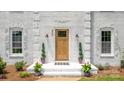 Charming white brick home entrance featuring a stylish wood door, modern lighting and greenery at 8337 Norcroft Dr, Charlotte, NC 28269