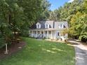 Expansive front lawn leading to a charming white home with dormer windows nestled among mature trees on a sunny day at 480 Robinson Rd, Mooresville, NC 28117