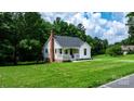 A charming cottage-style home with a brick chimney surrounded by a green lawn and lush trees at 2704 Kool Park Ne Rd, Hickory, NC 28601