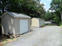 Backyard features two large sheds on a gravel lot next to the house and surrounding trees at 257 Rolling View Dr, New London, NC 28127