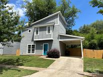 Modern gray home featuring a carport, a bright turquoise front door and tidy landscaping at 1534 Wembley Dr, Charlotte, NC 28205