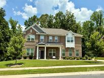 Charming brick two-story home featuring a manicured front lawn, mature trees, and welcoming front porch at 2044 Sweet William Dr, Harrisburg, NC 28075