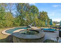 A beautiful in-ground pool and hot tub with a slide and lounge chairs are surrounded by lush greenery at 2657 Cheverny Pl, Concord, NC 28027
