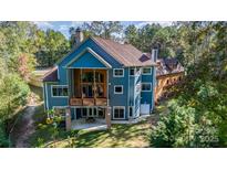 Stunning blue home featuring a spacious balcony, a patio, and surrounded by lush, mature trees at 1140 Fern Hill Rd, Mooresville, NC 28117
