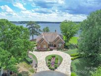 Stunning waterfront home featuring stone exterior, circular driveway, mature trees, and serene lake views at 18212 Pompano Pl, Cornelius, NC 28031