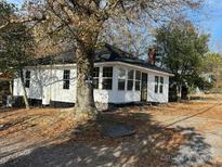 Charming home with a white exterior, black roof, brick chimney, and surrounding trees on a leaf-covered lot at 7608 Kershaw Camden Hwy, Kershaw, SC 29067