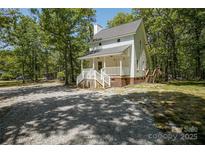 Charming white two-story home with a welcoming front porch and a spacious gravel driveway nestled in a wooded lot at 1062 Full Count Ln, Lancaster, SC 29720