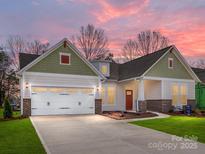 Inviting home exterior with green accents, a two-car garage, and a well-manicured lawn at sunset at 7169 Chamberlain Dr, Harrisburg, NC 28075