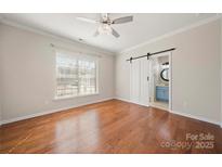 Bright bedroom with hardwood floors, ceiling fan, and sliding barn door to ensuite bathroom at 13929 Tilesford Ln, Huntersville, NC 28078