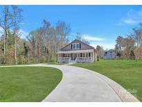 Inviting home features a circular driveway and a charming front porch, set against a backdrop of lush greenery at 12300 Caldwell Rd, Charlotte, NC 28213