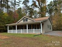 Ranch-style home with a large, inviting white-railed porch with brown siding and lush, mature trees at 369 Pinecrest Cir, Troy, NC 27371