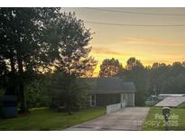 Charming single-story home with a well-maintained lawn, mature trees, and a colorful sunset in the background at 150 Windmill Ct, Harmony, NC 28634