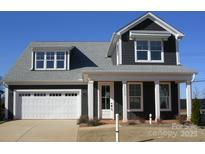 Charming two-story home featuring a white garage door, inviting front porch, and dark siding, perfect for modern living at 13618 Tranquil Day Dr, Matthews, NC 28105