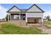 New construction with gray and white siding, brick foundation and attached two car garage with visible interior construction materials at 143 Tranquility Ln, Harmony, NC 28634