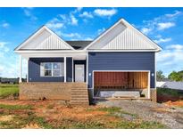 New construction exterior showing blue vinyl siding, white gables, brick foundation, and an attached open garage at 149 Tranquility Ln, Harmony, NC 28634