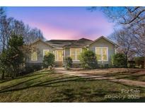 Inviting single-story home with a well-manicured lawn and mature trees, illuminated by warm lighting at 124 Muirfield Dr, Kings Mountain, NC 28086