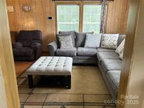 Inviting living room featuring wood paneling, plush gray sectional sofa, and a stylish tufted ottoman at 212 W Bingham St, Statesville, NC 28677