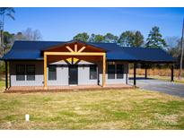 Gray metal siding home with black metal roof, covered porch, and carport at 411 E Gary St, Candor, NC 27229