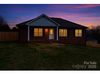 Charming brick home at dusk featuring a well-manicured lawn and warm light shining through the windows at 300 Pine Meadows Cir, Hickory, NC 28601